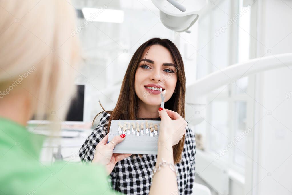 Beautiful young woman at dentist's office choose teeth color tone