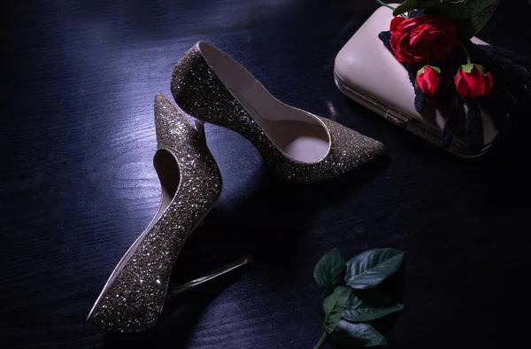 Altın rengi yüksek topuklu ayakkabılar. Koyu renkli bir masaya yakın plan. El çantası ve eldivenlerle.