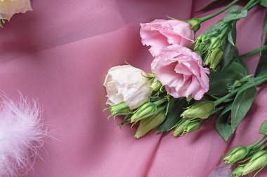 delicate twigs of flowers with buds on a pink silk background among white feathers. Romantic postcard