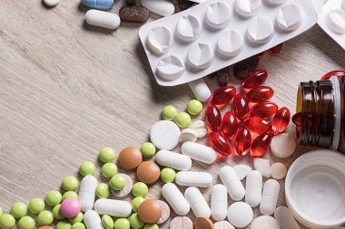 Tabletlerin çeşitli şekilleri ve renkleri masaya saçıldı. Boş ilaç paketleri ve ilaç şişesi.