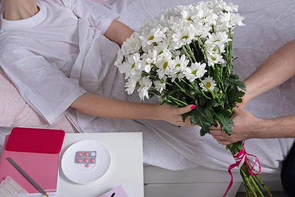 man gives flowers to sick girl. White chrysanthemums in male hands. Family care concept