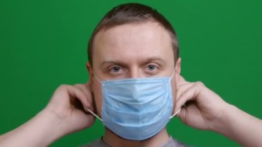 Yakın plan. Adam koruyucu bir tıbbi maske takıyor. Salgın virüsünün paniğinde. Koronavirüs salgını tehlikesi 2019-ncov. Yeşil izole bir arka planda çekilmiş. Karantina, korkular. Kromakey.