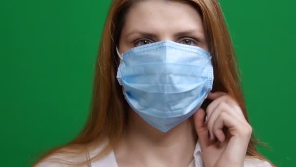 接近中だ。女の子は医療マスクを脱ぐ。笑顔だ。コヴィド。コロナウイルスのパンデミックの危険性2019-conv 。スタジオは緑の隔離された背景で撮影しました。隔離も恐怖も。クロマキー. — ストック動画