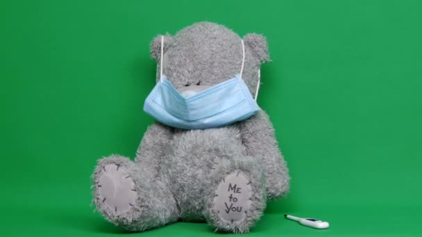 Teddybjörnen. En sjuk nallebjörn bär en medicinsk mask på ansiktet. Chroma nyckel. Grön bakgrund. Det är okej. COVID-19. Stockfilm