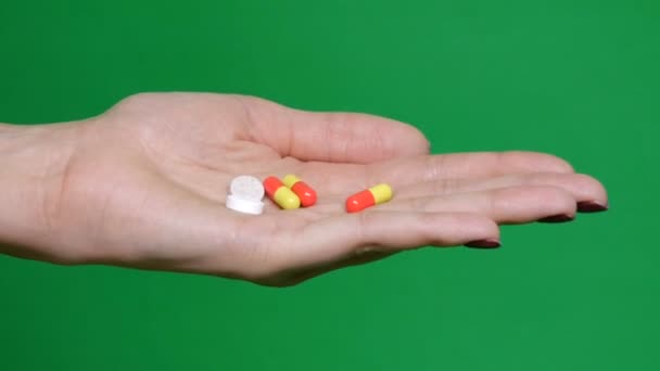 Různé druhy pilulky padající na zelené pozadí v ruce. Mnohobarevné tablety létají. COVID. Krásné kapky pilulky v ruce. Lékařské záběry, zdravý životní styl, vitamíny. Klíč Chroma. — Stock video