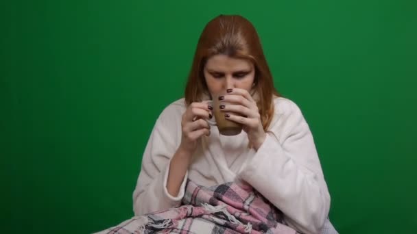 Close-up. Sick woman in a bathrobe wrapped in warm blanket drinking hot tea. COVID Danger of coronavirus pandemic 2019-ncov. Shot on a green isolated background. Quarantine, fears. Chromakey. — Stock Video