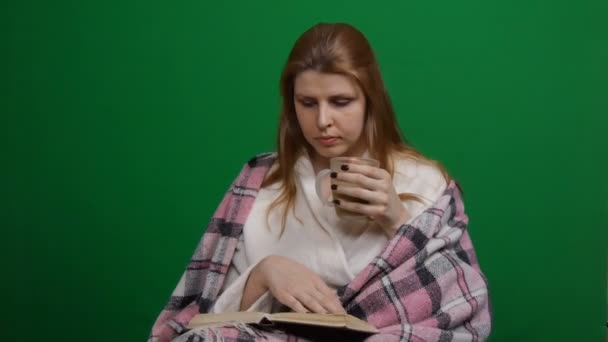 Sjuk kvinna insvept i varm filt som dricker hett te. COVID Läs boken. Fara för koronaviruspandemi 2019-ncov. Skjuten på en grön isolerad bakgrund. Karantän, rädsla. Chromakey Ordförande. — Stockvideo