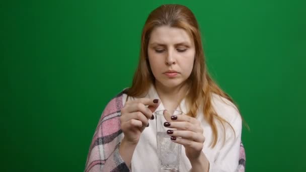 Kvinnan dricker ett brusande piller. Pillret droppar och löses upp med bubblor. COVID-19. brustablett i ett glas vatten på en grön bakgrund. Stockfilm