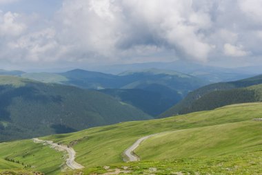 Yeşil çimenler ve bulutlarla kaplı dağ manzarası