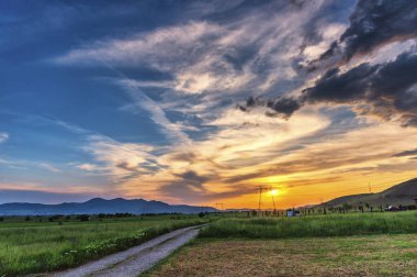 Güneş ve bulutlarla tarlanın üzerinde gün batımı