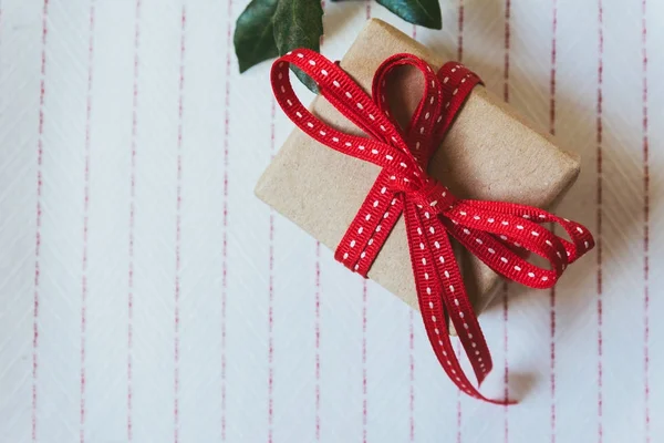 Caja de regalo, envuelta en papel reciclado y lazo rojo sobre tabla blanca —  Fotos de Stock