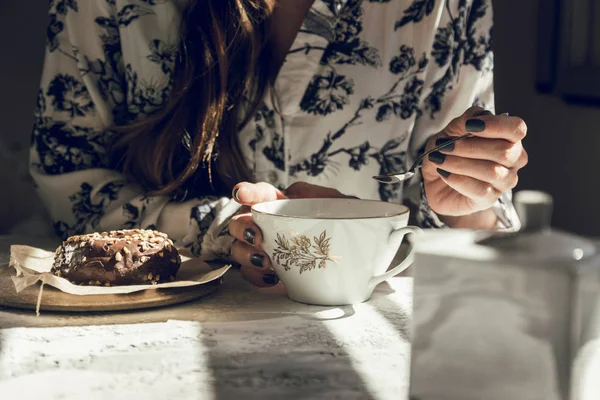 Mulher com xícara de chá, e donut de chocolate, sentado à mesa. b) — Fotografia de Stock