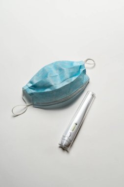 Beyaz arka planda cerrahi maske ve dijital termometre. Ağız ve burnu örtmek için tipik 3 katlı cerrahi maske. Sağlık ve Sağlık Hizmetleri