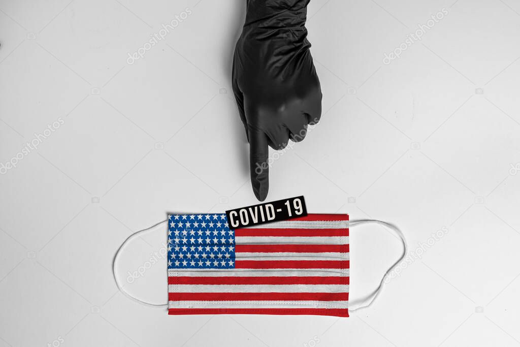 Doctors hand in black protective glove, points out surgical mask with the usa flag showing the message 