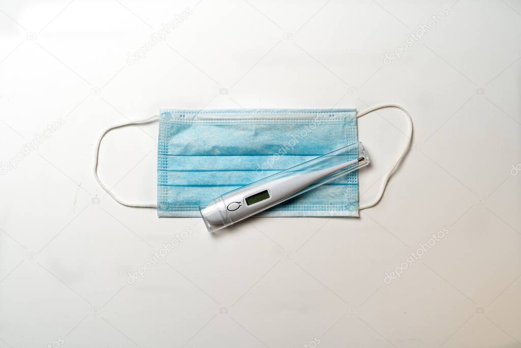 Surgical mask and digital thermometer on white background. Typical 3-ply surgical mask to cover the mouth and nose. Healthcare and medical conce