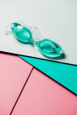 Pastel geometrik arka planda lastik kayışlı turkuaz yüzme gözlükleri. Hiç kimse, ürün konsepti