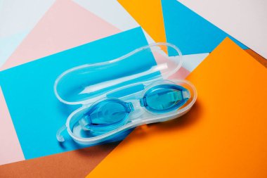 Turuncu ve turkuaz geometrik arka planda lastik kayışlı mavi yüzme gözlükleri. Hiç kimse, ürün konsepti