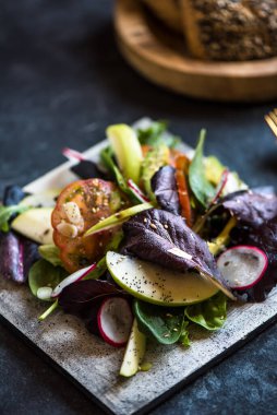 Lezzetli domates ve guacamole salatası, yeşil elma ve keten tohumlarıyla süslenmiş turp, koyu arkaplanda.