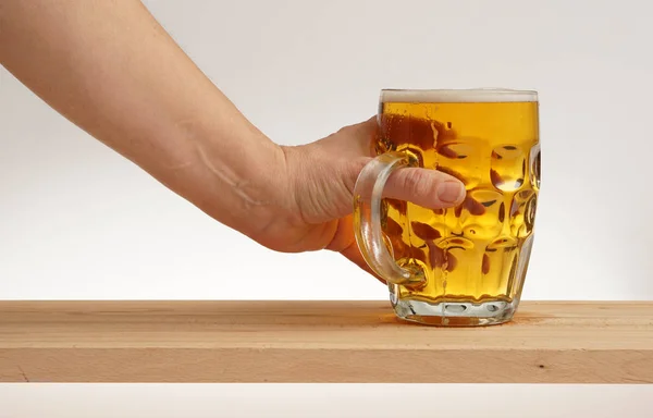 Mano tomar un vaso de cerveza ligera de tablero de madera . —  Fotos de Stock