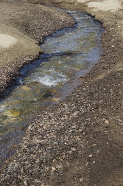 Çakıl taşları, kum ve kuru yapraklarla çevrili dağ deresi