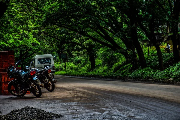 2019年9月13日インド コルハプール 木のトンネルのような緑の木で覆われたアスファルト道路のストックフォト 道路の2つの自転車駐車コーナー 前方に移動する白い色の車 インド コルハプールでモンスーンシーズン中に撮影された写真 — ストック写真