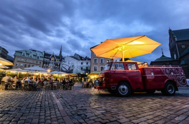 Riga, Letonya - 22 Ağustos 2017: Gece ışıkları, eski model kırmızı araba, eski binalar ve kafeterya, Riga, Letonya gece görüş Dome Meydanı. Riga şehir merkezi.