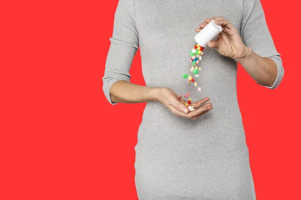 Обрезанный крупным планом образ женской руки выливает таблетки из бутылки, изолированной на красном фоне . — стоковое фото