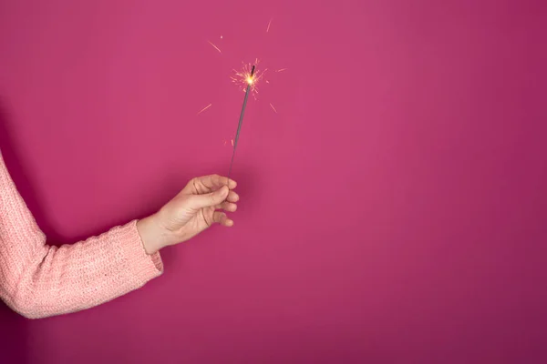 Close up of female hand with burning Christmas sparkler on pink background. Copy space — ストック写真