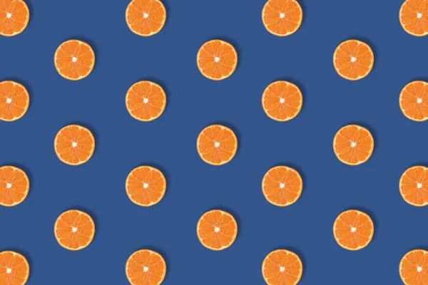 Fruit pattern of fresh bright orange citrus slices isolated on classic blue background. Flat lay, top view