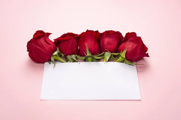 Party or wedding invitation. Red rose flowers arrangement with blank card, on light pink background