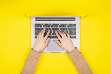 Yeni dizüstü bilgisayarda çalışan kadın eller. Parlak sarı arka planda. Üst manzara, düz yatış..