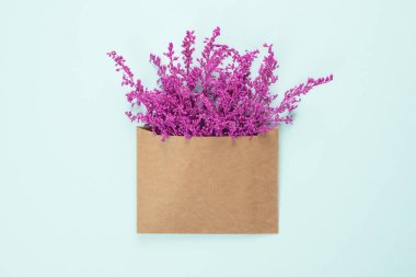 Açık mavi arkaplanda izole edilmiş fotokopi alanı olan el işi kahverengi zarf içinde parlak mor veya menekşe çiçekleri. Sevgililer Günü ya da Uluslararası Kadınlar Günü için modaya uygun pankart .