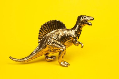 Sarı arka planda izole edilmiş altın oyuncak dinozor. Pop art monokrom konsepti.