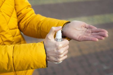 Genç bir kadın sokakta el dezenfektanı ile elleri dezenfekte ediyor. Coronavirus yayılan önlemler kavramı.