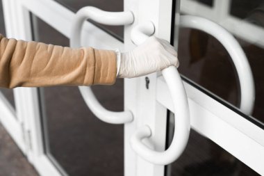 Kadın umumi bir yerde ya da sokakta kapıyı açar ve lateks koruyucu eldiven giyer. Coronavirus yayılan önlemler kavramı.