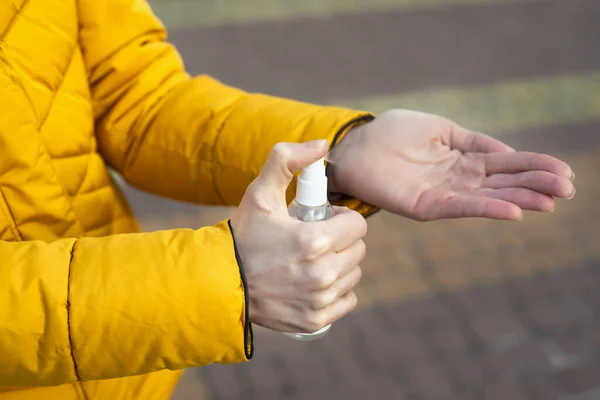 Young woman disinfects hands with a hand sanitizer on the street close up. Coronavirus spreading precautions measures concept.