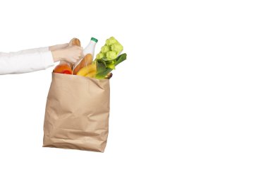 Yemek teslimatı ya da bağış konsepti. Market alışverişi. Kadın eli, meyve, sebze, süt, yoğurt, beyaz üzerine izole edilmiş yumurta gibi yiyeceklerle dolu bir kesekağıdı tutuyor..