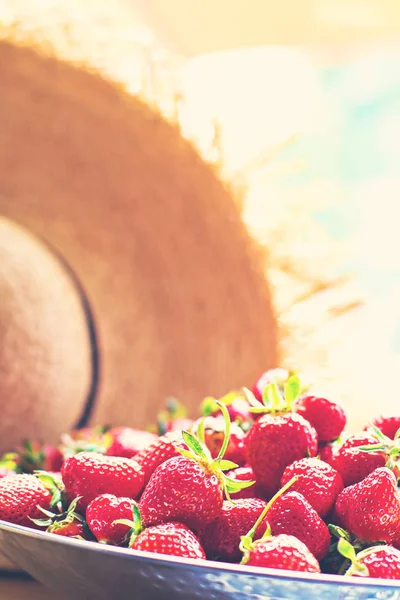 Gerechten met aardbeien en stro hoed in zonlicht. — Stockfoto