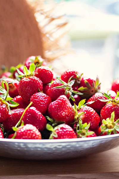 Gerechten met aardbeien en stro hoed in zonlicht. — Stockfoto