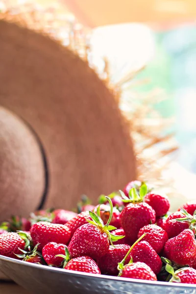 Gerechten met aardbeien en stro hoed in zonlicht. — Stockfoto
