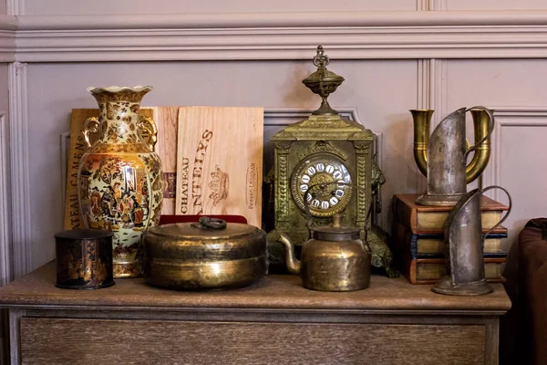 Chest of drawers, a regiment with ancient things. Ancient clock, a vase.