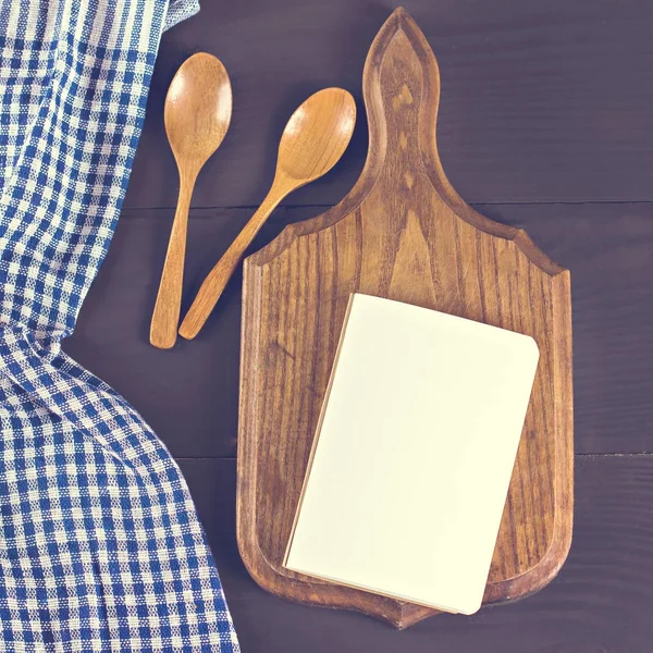 A blue kitchen towel and a notebook on a dark wooden background. Menu, place for text, recipe.