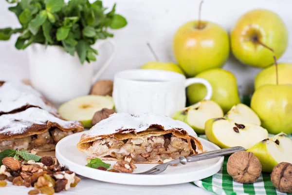 Ev yapımı elma strudel taze elma, tarçın, nane ve şeker tozu ile beyaz ahşap arka plan üzerinde hizmet dilimlenmiş. Yakın, karanlık rustik tarzı Apple strudel.