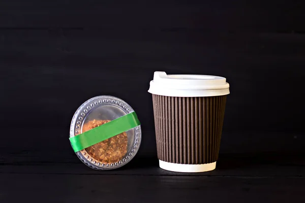 A paper cup with coffee and a box with biscuits