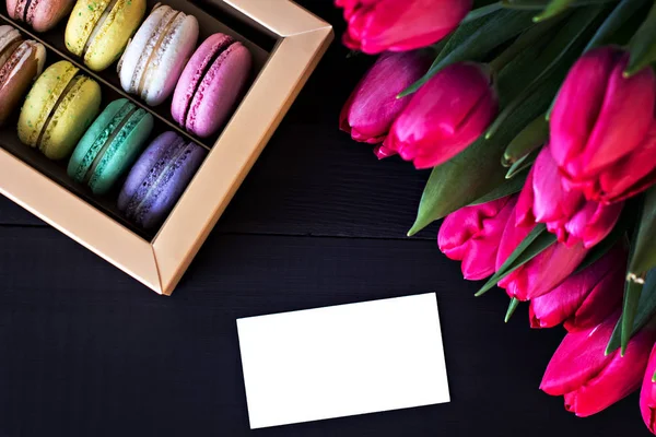 Box with macaroons and a bouquet of tulips and a card for your text on a dark background. — Stock Photo, Image