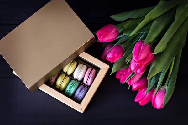 Box with macaroons and a bouquet of tulips and a card for your text on a dark background. — Stock Photo, Image