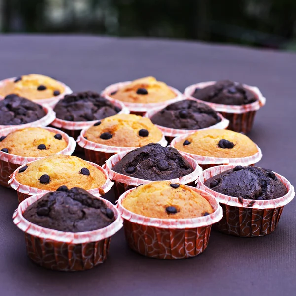 Pastel de chocolate y cupcakes de vainilla con gotas de chocolate sobre la mesa . —  Fotos de Stock