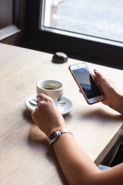Close-Up fincan kahve ile oturan kadının elinde cep telefonu. 