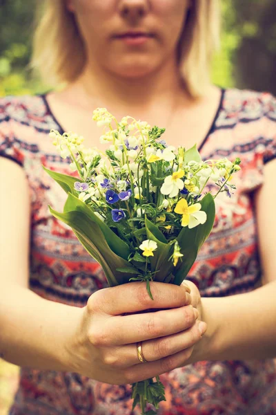 Een boeket van lelies van de vallei en het bos viooltjes in de hand van een vrouw. — Stockfoto