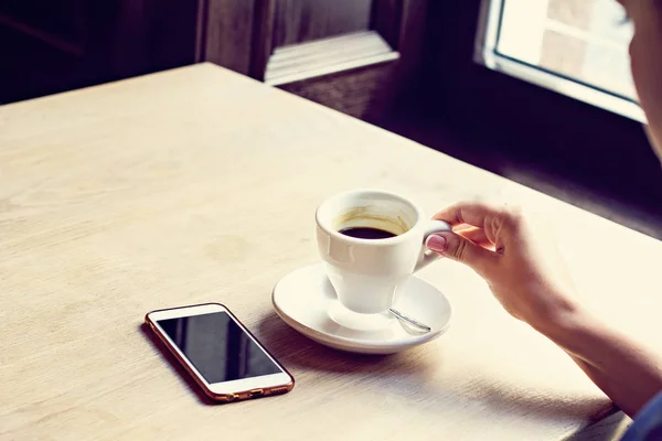 Primo piano del telefono cellulare nelle mani della donna, seduto con una tazza di caffè . — Foto Stock